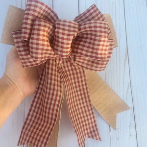 May include: A red and white gingham bow with a burlap tail. The bow is tied in a large, full knot.