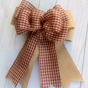 May include: A red and white gingham bow with a burlap bow tail. The bow is tied with a knot in the center and has two tails.