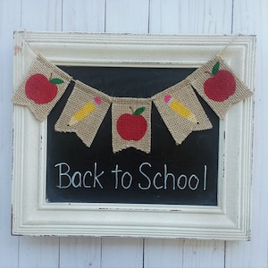 May include: A burlap banner with alternating red apples and yellow pencils, hanging on a chalkboard with the text "Back to School".