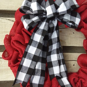 May include: A red burlap wreath with a large black and white checkered bow. The bow is tied with a large knot and the tails are long and flowing.