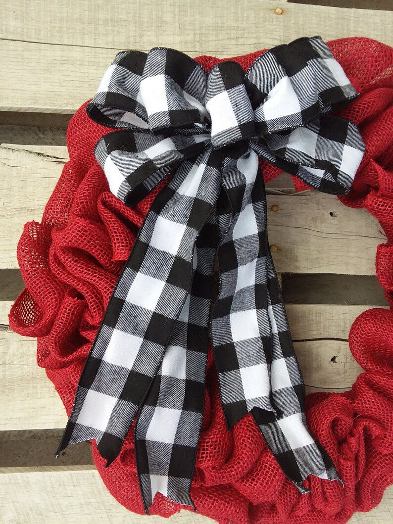 May include: A red burlap wreath with a large black and white checkered bow. The bow is tied with a large knot and the tails are long and flowing.