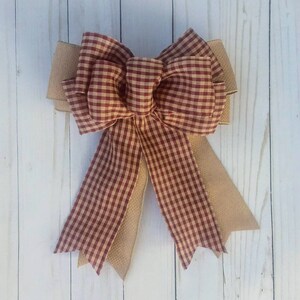 May include: A large, red and tan gingham bow with a burlap center. The bow is tied with a loop and is ready to be used as a decorative element.