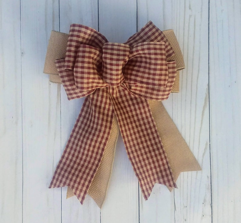 May include: A large, red and tan gingham bow with a burlap center. The bow is tied with a loop and is ready to be used as a decorative element.