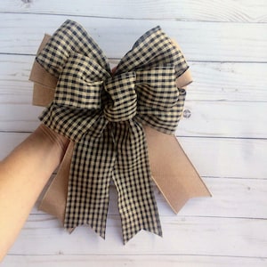 May include: A large black and tan gingham bow with a burlap backing. The bow is tied with a loop and is ready to be hung.