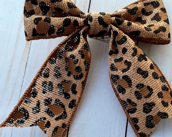 May include: A brown and black leopard print burlap bow. The bow is tied with a wire loop for hanging.