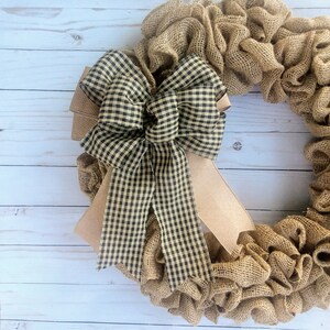 May include: A brown burlap wreath with a large black and white gingham bow. The wreath is made of burlap and has a rustic look.