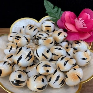May include: A bowl of white and black tiger-striped shell beads. The beads are arranged in a random pattern and are surrounded by a pink flower.