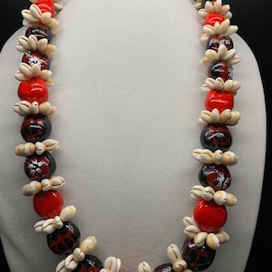 May include: A traditional Hawaiian lei necklace made with white and black shell beads and red beads. The shell beads have a floral design.