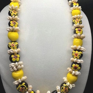 May include: A yellow and black lei with white flower accents. The lei is made of round beads with painted flowers and small white shell beads.