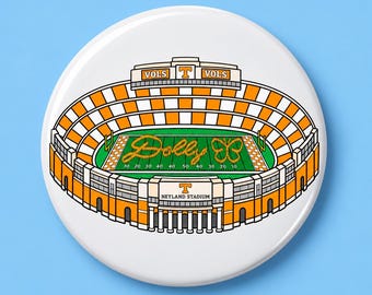 May include: A circular pin featuring an illustration of Neyland Stadium with orange and white checkered seating. The green field displays the script text Dolly and a butterfly graphic. The stadium exterior is labeled VOLS and NEYLAND STADIUM.