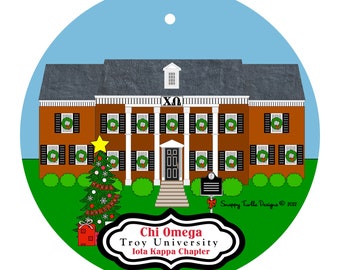 May include: A round Christmas ornament featuring a brick building with white columns and black shutters, decorated with wreaths. A Christmas tree and gift are in the foreground. The text reads "Chi Omega Troy University Iota Kappa Chapter."