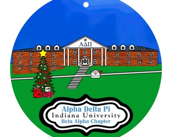 Könnte beinhalten: Runder Weihnachtsschmuck mit einem Gebäude mit den griechischen Buchstaben ΑΔΠ. Ein geschmückter Weihnachtsbaum und Geschenke befinden sich links. Der Text "Alpha Delta Pi Indiana University Beta Alpha Chapter" steht unten.