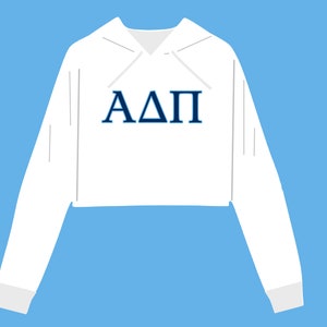 May include: White cropped hoodie with the Greek letters ΑΔΠ in navy blue across the chest. The hoodie has a drawstring and long sleeves with ribbed cuffs. The background is a light blue.