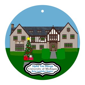 May include: A round Christmas ornament featuring a detailed illustration of a building with a Christmas tree and gifts. The ornament has a blue sky background and green grass. Text on the ornament reads: Alpha Tau Omega, University of Michigan, Beta Lambda Chapter.