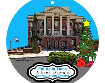 May include: Round Christmas ornament featuring a building with columns, a decorated Christmas tree, and gifts. The ornament has a blue background and text that reads "Phi Delta Theta Athens, Georgia Georgia Alpha Chapter."