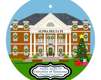 May include: A round Christmas ornament featuring a brown building with white columns and the text "ALPHA DELTA PI". The building is decorated with wreaths and a Christmas tree. The text "Alpha Delta Pi, University of Tennessee, Alpha Kappa Chapter" is also present.