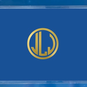 May include: Clear acrylic serving tray with a vibrant blue interior. The tray features gold-colored handles and a gold monogram in the center. The monogram consists of the letters "JLJ" inside a gold circle. A stylish and functional home decor item.