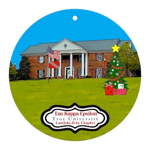 May include: Round Christmas ornament featuring a brick building with white columns, flags, and a decorated Christmas tree. The ornament has the text "Tau Kappa Epsilon, Troy University, Lambda-Zeta Chapter" in a decorative frame.