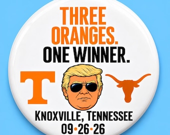May include: A round white pinback button featuring the orange text THREE ORANGES. ONE WINNER. above a cartoon illustration of a person with blonde hair and sunglasses, flanked by an orange letter T and a longhorn logo, with KNOXVILLE, TENNESSEE 09-26-26.