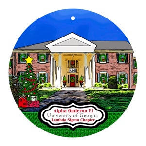 May include: A round Christmas ornament featuring a brick building with white columns and a Christmas tree. The ornament has the text "Alpha Omicron Pi University of Georgia Lambda Sigma Chapter" in a decorative frame. The background is blue.