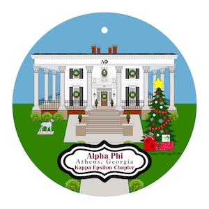 May include: A round Christmas ornament featuring a white house with columns, wreaths, and a decorated Christmas tree. The ornament has the text "Alpha Phi Athens, Georgia Kappa Epsilon Chapter" in a black and white frame.