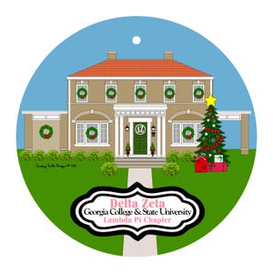 May include: A round Christmas ornament featuring a house decorated for the holidays. The house is tan with a red roof, green wreaths, and a Christmas tree. The ornament has the text "Delta Zeta Georgia College & State University Lambda Pi Chapter."