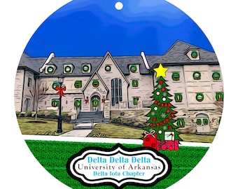 May include: A round Christmas ornament featuring a building with a Christmas tree and gifts. The ornament has the text "Delta Delta Delta University of Arkansas Delta Iota Chapter" in a white and black design.