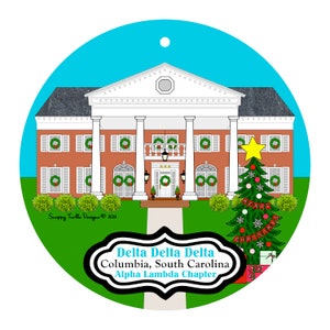 May include: A round Christmas ornament featuring a brick building with white columns and shutters, decorated with wreaths. A Christmas tree with a star and "Merry Christmas" banner stands to the right. The ornament includes the text "Delta Delta Delta, Columbia, South Carolina, Alpha Lambda Chapter."