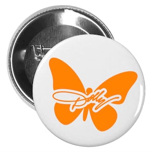 May include: A circular pin-back button featuring a white background with a solid orange butterfly graphic centered on the front. The word Dolly is written in a white cursive script font across the center of the orange butterfly wings.