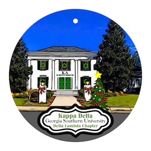 May include: A round Christmas ornament featuring a white building with green wreaths and a Christmas tree. The ornament has the text "Kappa Delta Georgia Southern University Delta Lambda Chapter" in a decorative frame. A blue sky background.