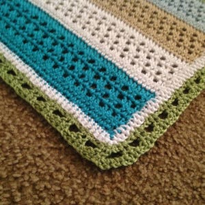 May include: A crocheted blanket with stripes of teal, white, and beige. The blanket has a green crocheted border.