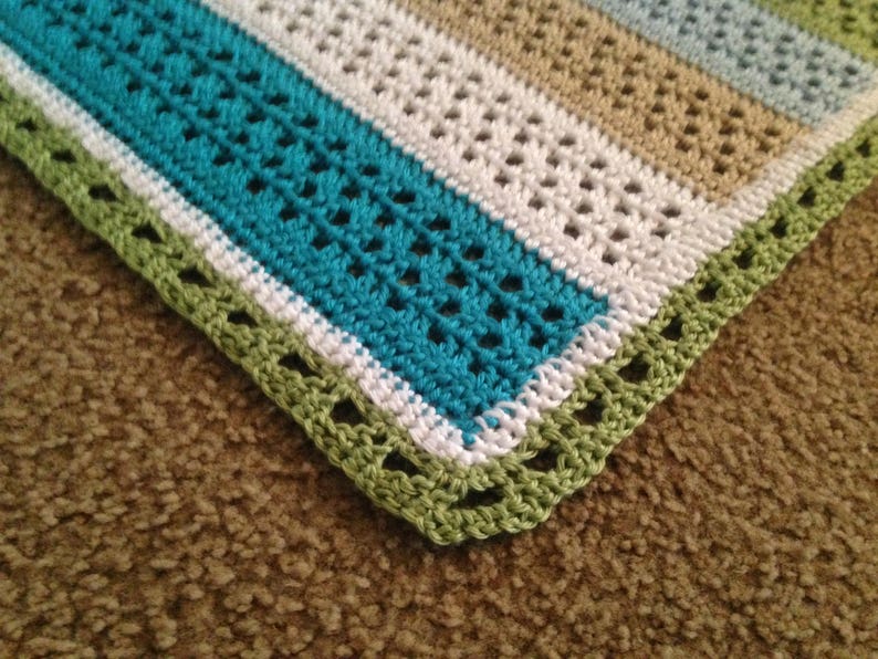 May include: A crocheted blanket with stripes of teal, white, and beige. The blanket has a green crocheted border.
