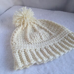 May include: A white crocheted beanie with a fluffy white pom pom on top.