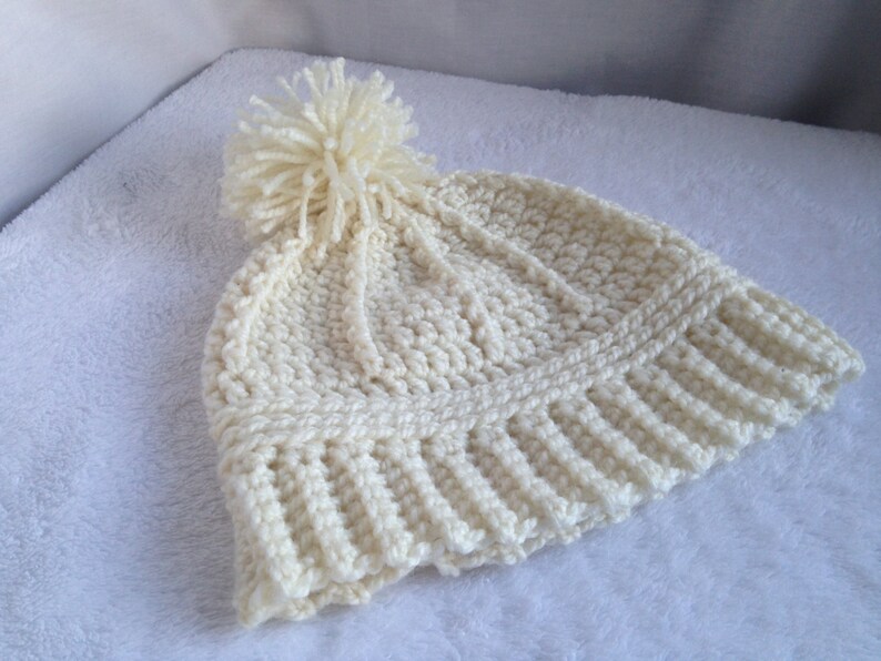 May include: A white crocheted beanie with a fluffy white pom pom on top.