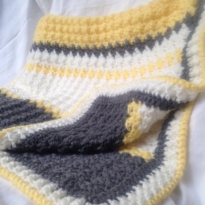 May include: A crocheted baby blanket in yellow, white, and gray with a textured stitch pattern.