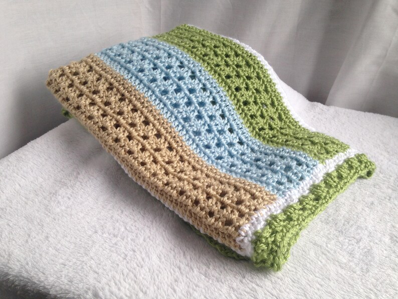 May include: A crocheted baby blanket with stripes of tan, light blue, white, and green.
