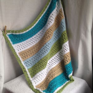 May include: A crocheted baby blanket with stripes of white, teal, light blue, green, and tan.