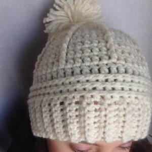 May include: White crocheted beanie with a white pom pom on top.