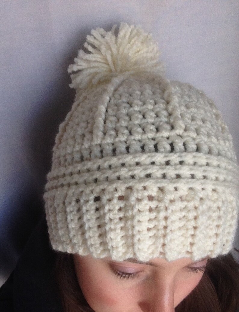May include: White crocheted beanie with a white pom pom on top.