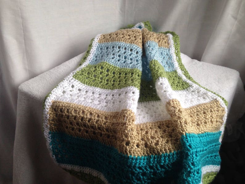 May include: A crocheted baby blanket with stripes of white, tan, green, blue, and teal.