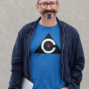 May include: A blue t-shirt with a black triangle and a white "C" containing a red and blue atom design. The person is wearing a navy blue jacket, blue jeans, and glasses, holding a silver laptop.