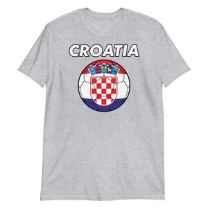 May include: A light gray t-shirt featuring the word "CROATIA" in white block letters above a soccer ball design. The soccer ball is in the colors of the Croatian flag, with a red and white checkered pattern.