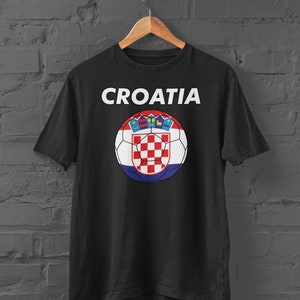 May include: Black t-shirt featuring the word "CROATIA" in white above a soccer ball design. The soccer ball incorporates the Croatian flag's red and white checkered pattern, along with the Croatian coat of arms.