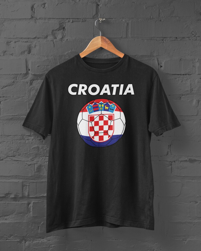 May include: Black t-shirt featuring the word "CROATIA" in white above a soccer ball design. The soccer ball incorporates the Croatian flag's red and white checkered pattern, along with the Croatian coat of arms.