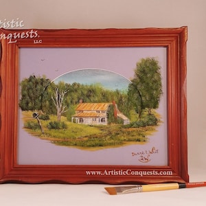 May include: A framed painting of a rural farmhouse with a rusty metal mailbox in the foreground. The painting is in a red wooden frame and has a light blue background. The artist's signature, "Duane L. West", is visible in the bottom right corner. The website address, "www.ArtisticConquests.com", is also visible below the signature.