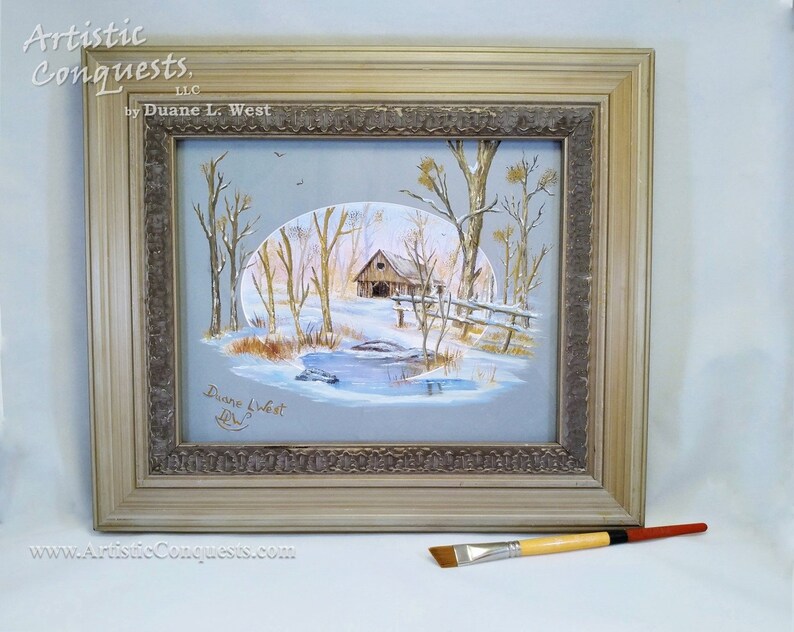 May include: A framed painting of a winter scene with a cabin, trees, and a pond. The painting is signed "Duane L. West" in the bottom left corner. The frame is a light brown color with a decorative border. The painting is titled "Artistic Conquests, LLC by Duane L. West".