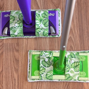 May include: Two green and white patterned microfiber mop pads with the word "Swiffer" printed on the top pad. The pads are attached to a purple and green mop handle.