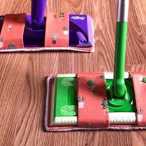 May include: Two Swiffer mop heads with custom fabric covers. The covers are orange with a green and white floral pattern. One mop head is purple and the other is green.