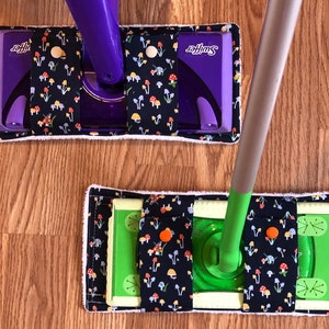 May include: Two Swiffer mop pads with a mushroom print. The top pad is purple and the bottom pad is green. Both pads have a white border.
