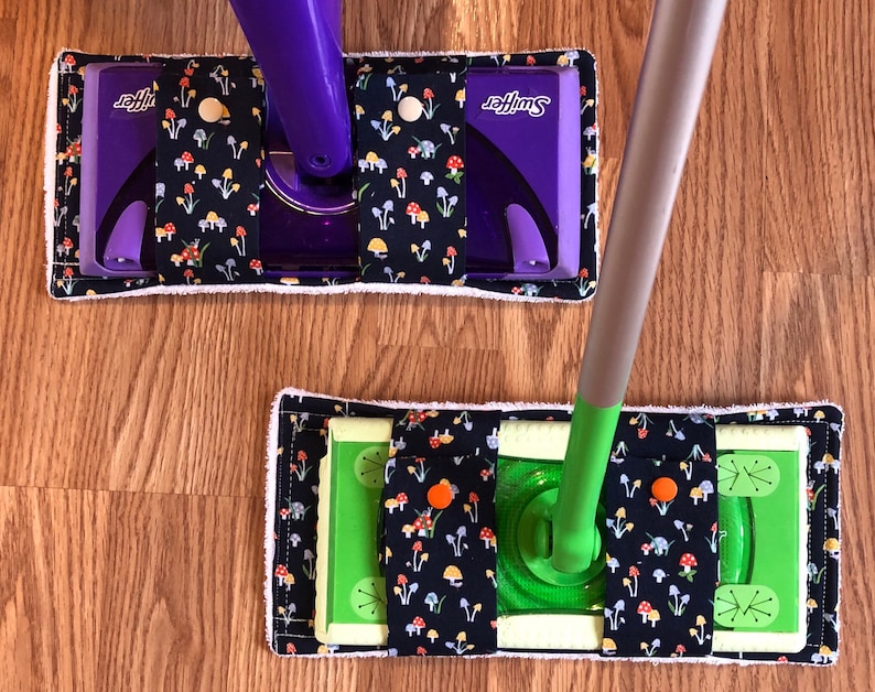 May include: Two Swiffer mop pads with a mushroom print. The top pad is purple and the bottom pad is green. Both pads have a white border.